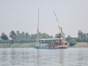 A beautiful sailboat glides through calm waters, surrounded by lush greenery, showcasing the serene atmosphere of a river cruise.