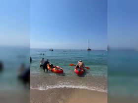Two kayakers prepare to launch from the beach while others enjoy the clear waters — a perfect day for water activities and fun in the sun.