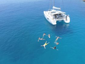 A lively group enjoys a refreshing swim in crystal-clear waters near a catamaran, capturing the essence of a perfect day on the water.
