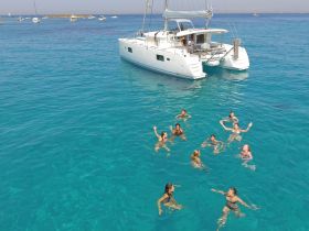A lively group enjoys a refreshing swim in crystal-clear waters near a catamaran, capturing the essence of fun and relaxation on a perfect day at sea.