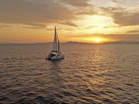 A stunning aerial view of a catamaran sailing at sunset, surrounded by tranquil waters and distant islands, perfect for showcasing serene sailing experiences.