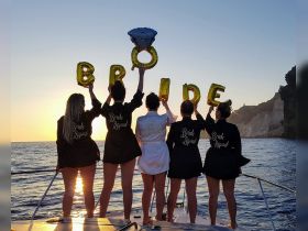 A joyful group of bridesmaids celebrates the bride-to-be at sunset, holding balloons that spell 'BRIDE' — a perfect moment for bachelorette parties on the water.