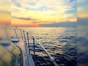 A stunning sunset view from the bow of a boat, showcasing tranquil waters and distant sailboats — perfect for evening cruises.