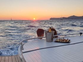 A couple enjoys a romantic sunset on a boat, complete with cocktails and a platter of snacks — the perfect setting for a memorable dinner cruise.