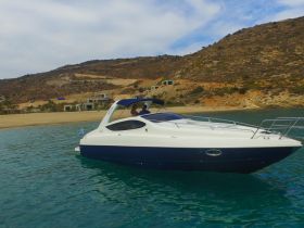 A sleek speedboat is anchored in calm waters, showcasing its elegant design against a scenic backdrop of hills and beach — perfect for day trips and coastal exploration.