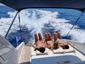 Three friends enjoy sunbathing on the deck of a yacht, soaking up the summer sun while cruising through beautiful blue waters.
