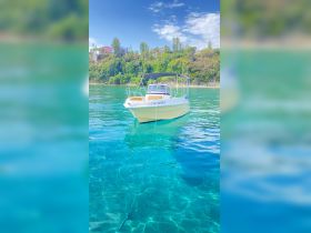 A charming boat named 'ΟΔΥΣΣΕΥΣ' anchored in crystal-clear waters, surrounded by lush greenery — perfect for a day of exploration and relaxation on the water.