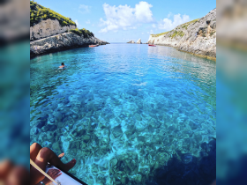 A serene view of a swimmer enjoying the crystal-clear waters surrounded by stunning cliffs — a perfect destination for a relaxing day on the water.