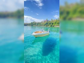 A beautiful boat floats serenely in crystal-clear waters, showcasing the vibrant colors of the sea and surrounding greenery — perfect for exploring coastal destinations.