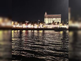 A nighttime view of a waterfront scene with illuminated buildings and reflections on the water, creating a serene atmosphere.