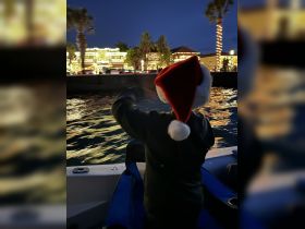 A child in a Santa hat enjoys the festive lights along the waterfront from a boat at night, capturing the holiday spirit on the water.