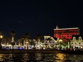 A picturesque waterfront scene illuminated by festive lights at night, showcasing a charming coastal town atmosphere perfect for evening boat tours.