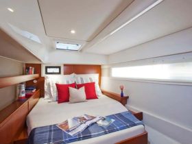 Cozy interior cabin of a boat featuring a comfortable bed with decorative pillows and natural light streaming in through the windows, perfect for relaxing during a sailing trip.