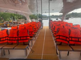 Interior view of a boat featuring rows of bright orange life jackets on the seating, showcasing safety preparations for passengers on a Krabi boat trip.