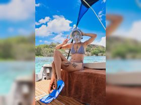 A woman poses with a snorkel mask and fins on a boat, ready for an exciting snorkeling adventure in crystal-clear waters.
