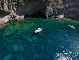 An aerial view captures a stunning coastline with a boat anchored nearby, while snorkelers explore the vibrant underwater scenery — a perfect day for adventure on the water.