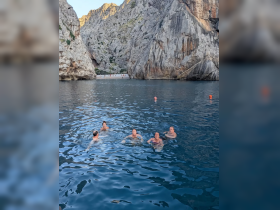 A lively group enjoys swimming in a stunning cove surrounded by rocky cliffs, capturing the essence of adventure and relaxation in nature.
