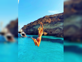 A woman joyfully jumps into the crystal-clear waters, capturing the essence of summer fun and adventure aboard a boat.