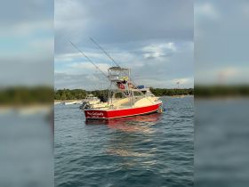 A vibrant fishing boat named 'May Caliente' is anchored in calm waters, showcasing its sleek design and fishing gear, perfect for ocean adventures.