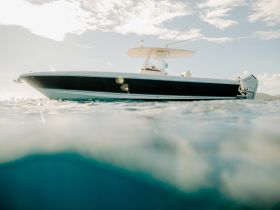 A sleek speedboat captured from below the water's surface, showcasing its elegant design against a backdrop of clear skies and shimmering water.