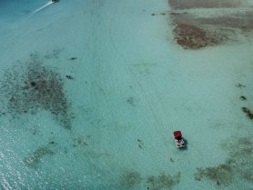 Aerial view of a boat anchored in shallow turquoise waters, with people enjoying a sandbar stop — perfect for a fun day on the water.