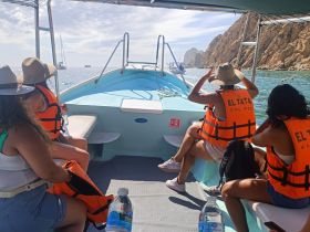 A group of friends wearing life jackets enjoys a scenic boat ride in Cabo San Lucas, capturing the beauty of the ocean and surrounding cliffs.