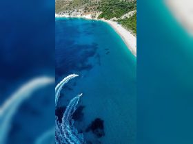 A stunning aerial view of a serene beach with crystal-clear waters and boats cruising along the coastline, perfect for showcasing the beauty of a summer getaway.