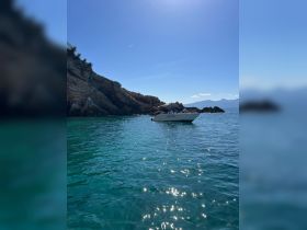 A sleek speedboat anchored in crystal-clear waters near rocky cliffs, perfect for exploring coastal destinations.