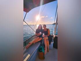 Two friends enjoy cocktails on a boat at sunset, capturing a perfect moment of relaxation and celebration on the water.