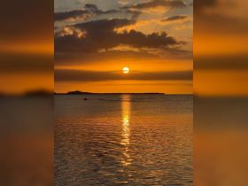 A breathtaking sunset casts golden hues over the water, with a distant island silhouette creating a serene backdrop — perfect for capturing the beauty of nature.