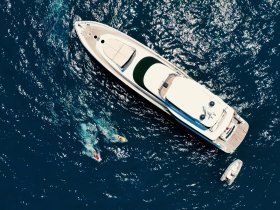 Aerial view of a luxurious yacht with two individuals swimming nearby, showcasing the perfect blend of relaxation and adventure on the water.