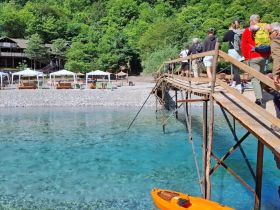 A lively group walks along a wooden pier towards a beautiful beach with clear turquoise waters, perfect for kayaking and relaxation.