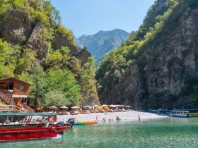 A vibrant scene at a beach with visitors enjoying the clear waters and a red boat nearby, perfect for a fun day out in nature.