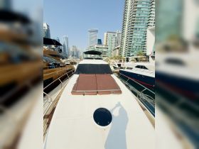 A sleek yacht docked in a marina, showcasing its spacious deck and luxurious design against a backdrop of modern skyscrapers.