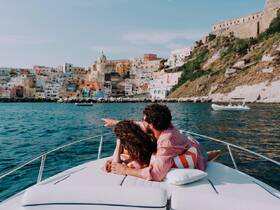 A couple enjoys a scenic view from their boat, pointing towards the colorful coastal town — a perfect moment for romantic getaways and exploration.
