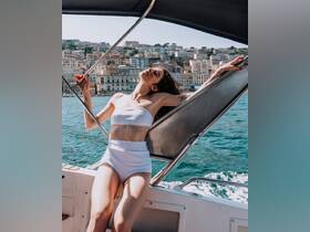 A woman enjoys the sun on a boat, with picturesque coastal scenery in the background — perfect for summer outings and relaxation on the water.