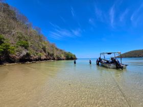 A serene scene of individuals fishing in shallow waters near a boat, surrounded by lush greenery and a clear blue sky — perfect for outdoor adventures and fishing trips.