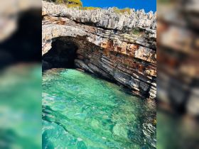 A stunning view of a rocky coastline with a natural arch, surrounded by crystal-clear turquoise waters — a perfect spot for exploration and adventure.