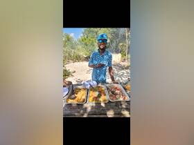 A chef presents a delicious spread of food on a beach, showcasing a variety of dishes perfect for catering during a boat trip or beach outing.