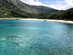 A stunning view of a tranquil beach with crystal-clear turquoise waters and lush green hills in the background, perfect for a serene getaway or island exploration.