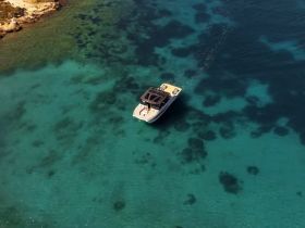 Aerial view of a sleek boat cruising through crystal-clear turquoise waters, showcasing the beauty of the surrounding marine environment.