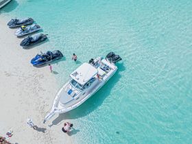 A vibrant scene at the beach with a group enjoying jet skis and swimming in crystal-clear waters, perfect for a fun day on the water.