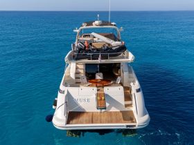 A stunning aerial view of the yacht 'Muse' cruising through crystal-clear waters, showcasing its elegant design and spacious deck — perfect for luxury charters.