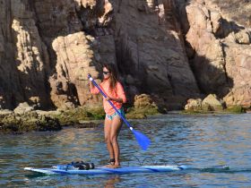 A woman paddleboards in calm waters near rocky cliffs, showcasing the thrill of water sports and the beauty of nature.