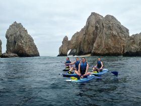 A group of friends enjoys kayaking near stunning rock formations, showcasing the beauty of the coastline — an ideal adventure for water enthusiasts.