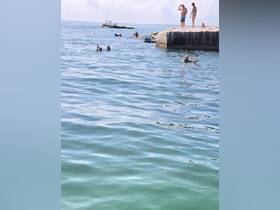 A lively scene of people enjoying a sunny day at the beach, swimming and relaxing in the clear waters — perfect for summer fun and group outings.