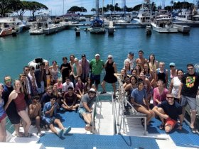 A large group gathers on the deck of a boat at the harbor, showcasing a fun and vibrant atmosphere perfect for group outings and celebrations.