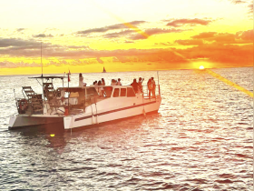 A lively group enjoys a sunset cruise aboard a boat, capturing the essence of celebration on the water as the sun sets on the horizon.