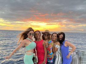 A joyful group of friends poses against a stunning sunset backdrop while enjoying their time on the water — perfect for memorable celebrations and gatherings.