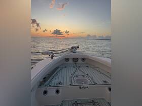 A serene view from the front of a Blackjack boat as the sun sets over calm waters, showcasing the vessel's sleek design against a vibrant sky.